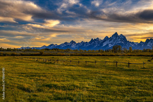 Colorful sunset above the Grand Teton mountains in Wyoming with a wooden fence in the foreground.