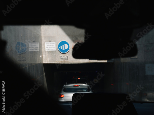 The entrance to a Spanish underground garage featuring a dedicated sign that instructs drivers to keep their lights on at all times, displaying 'En Tot El Recinte' for added safety photo