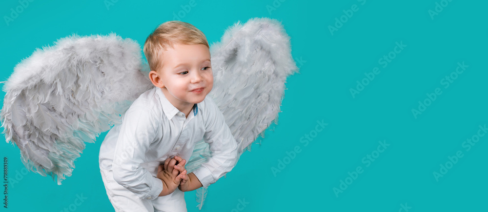 Valentines day banner with angel child. Child angel. Small cute baby boy with blonde hair in white feathered angel wings on blue background. Valentines day banner with angel child. Child angel. Small cute baby boy with blonde hair in white feathered angel wings on blue background.