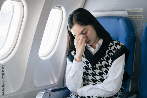 Tired asian woman with headache feeling sick while sitting in the airplane , Passengers near the window. photo