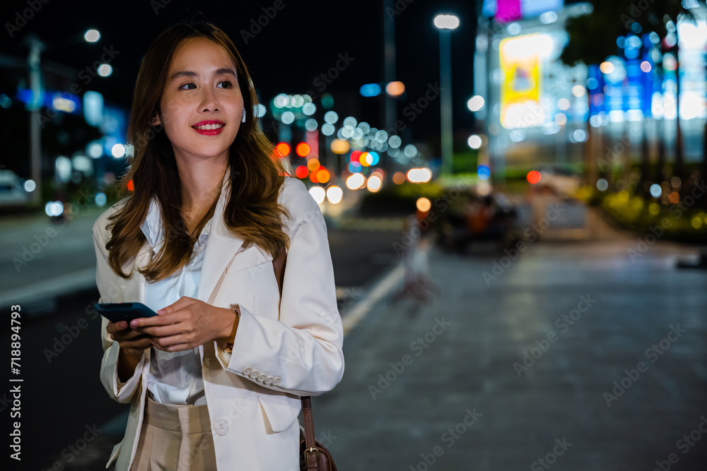 Fototapeta premium Stylish blogger woman walking in autumn city streets and texting on smartphone at night. Urban technology lifestyle concept.
