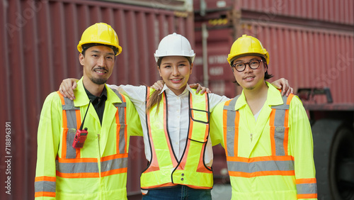 Group of asian engineers and workers wearing safety vests uniform and helmets standing with arm around shoulder and looking at camera. Logistic distribution, Teamwork concept