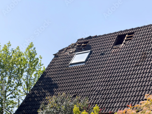 View of a damaged house roof with visible holes and missing tiles, indicating a need for urgent repairs.
