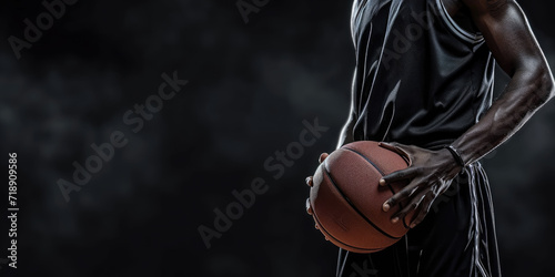 A focused athlete in a dark jersey holds a basketball against a dark background, emphasizing the readiness and determination for the game.	
 photo