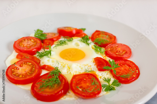 hearty breakfast. on a white plate lies one fried egg, around it lies a sliced red tomato sprinkled with herbs, breakfast concept