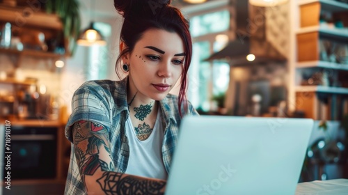 A stylish woman with bold tattoos on her arm sits indoors, gazing intently at her laptop, her fashionable clothing adding to the overall aesthetic of the scene