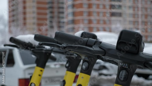 Close-up of urban electric scooter rentals stand in a row in the city in snowy winter weather. Electric scooters covered with snow in urban areas. Ecotransport in winter. photo