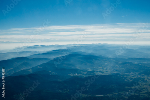 A breathtaking aerial view of rolling mountain ranges blanketed in mist, contrasting against a serene blue sky filled with gentle cloud