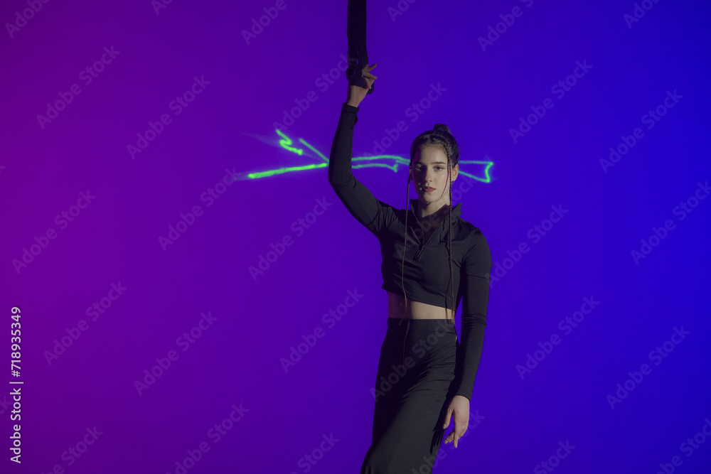 Young acrobat poses with rope in hand in studio with purple light. Gymnast girl in black costume prepare for performance.