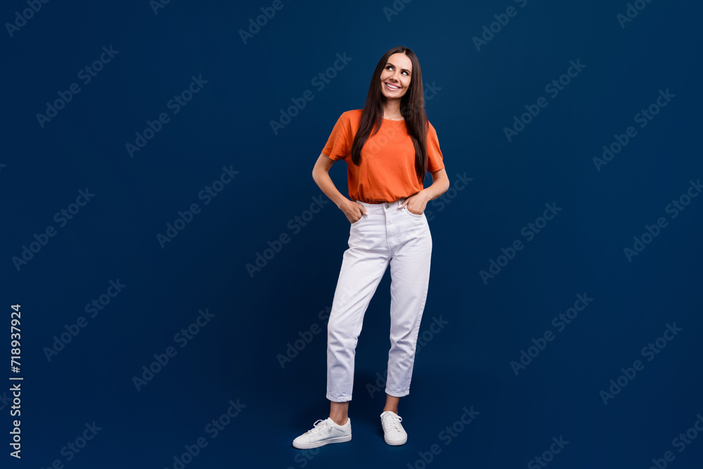 Full length photo of sweet dreamy lady wear orange t-shirt looking empty space isolated dark blue color background