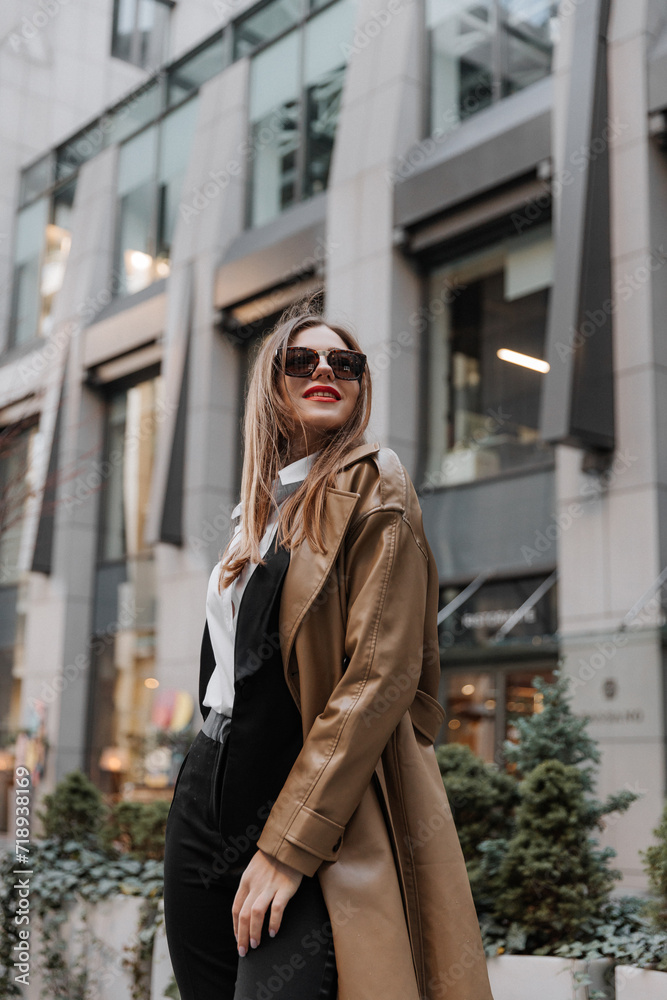 Fototapeta premium Outdoor portrait of a beautiful young businesswoman in a brown coat at the city