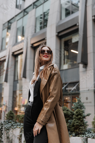 Outdoor portrait of a beautiful young businesswoman in a brown coat at the city © Ankor_stock.