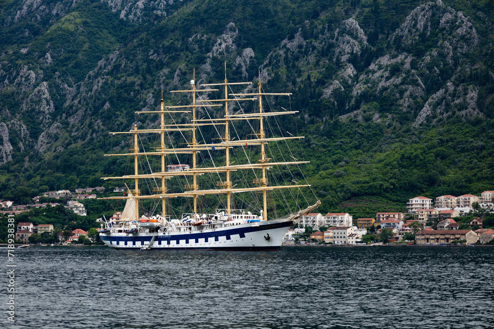 Kotor, Montenegro - 06 17 2023: A sail cruise ship in a bay with the mountains and traditional architecture Kotor houses in the background Kotor, Montenegro - 06 17 2023: A sail cruise ship in a bay with the mountains and traditional architecture Kotor houses in the background
