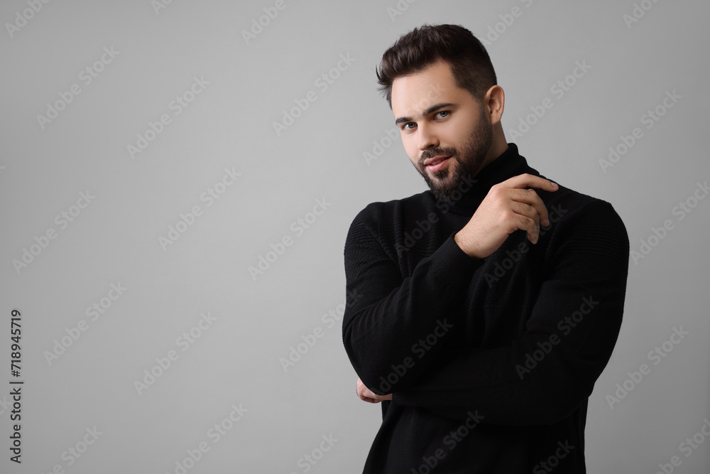 Handsome man in stylish black sweater on grey background, space for text
