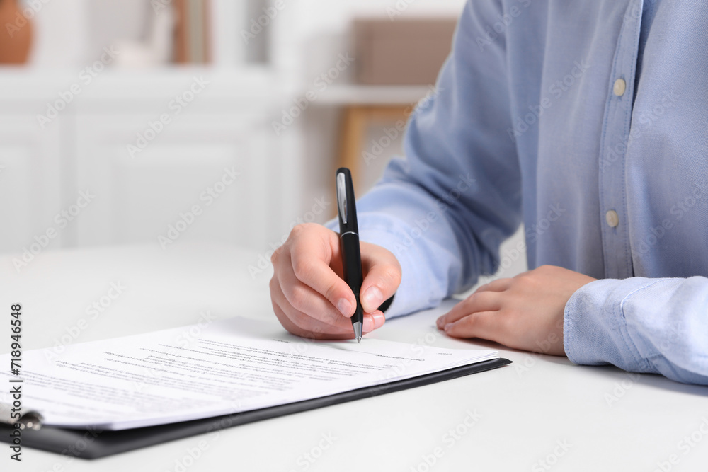 Woman signing document at white table indoors, closeup. Space for text Woman signing document at white table indoors, closeup. Space for text