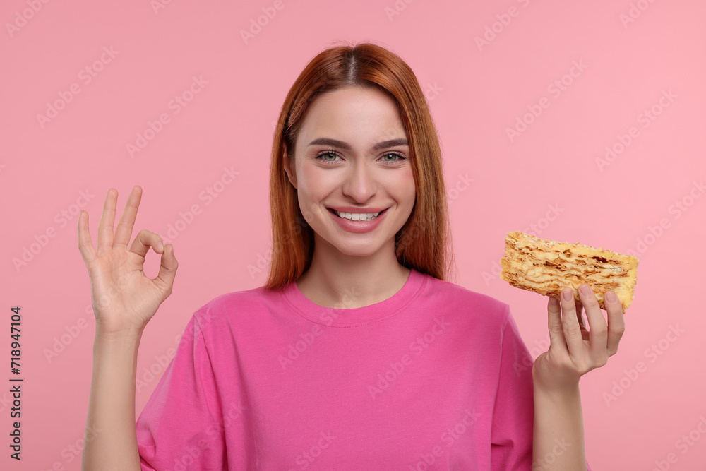 Young woman with piece of tasty cake showing ok gesture on pink background Young woman with piece of tasty cake showing ok gesture on pink background