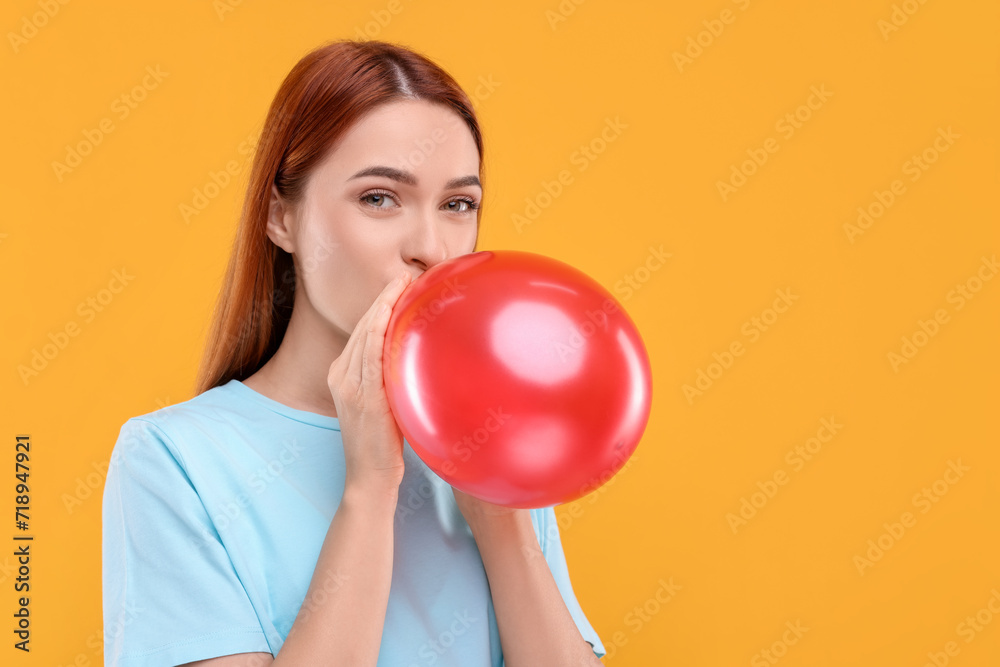 Woman inflating red balloon on orange background, space for text Woman inflating red balloon on orange background, space for text