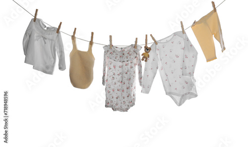 Different baby clothes and toy bear drying on laundry line against white background photo