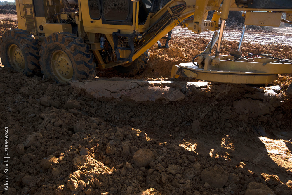 Road grader is pushing dirt. Motor grader is working,smoothing gravel surface for new road.