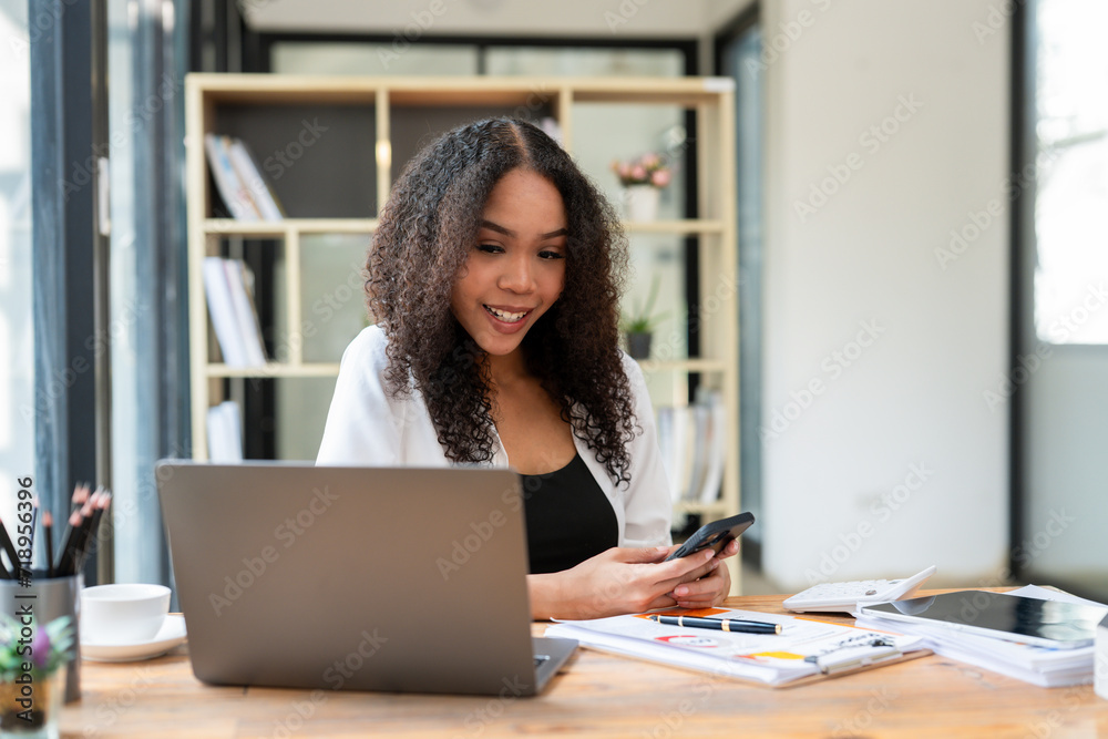 Smiling black businesswoman using smartphone while working on laptop. Smiling black businesswoman using smartphone while working on laptop.