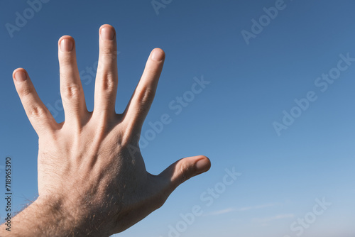 Hand doing showing number five gesture on blue sky background. Gesturing number 5. Number five in sign language. Fifth, counting down five concept. Five fingers up. 