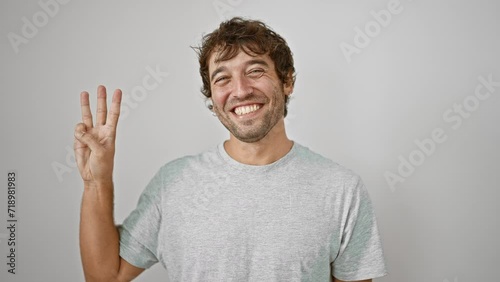 Confident young man, pointing up showing number three with fingers, happy smile brightening up his casual t-shirt look on white isolated background. photo