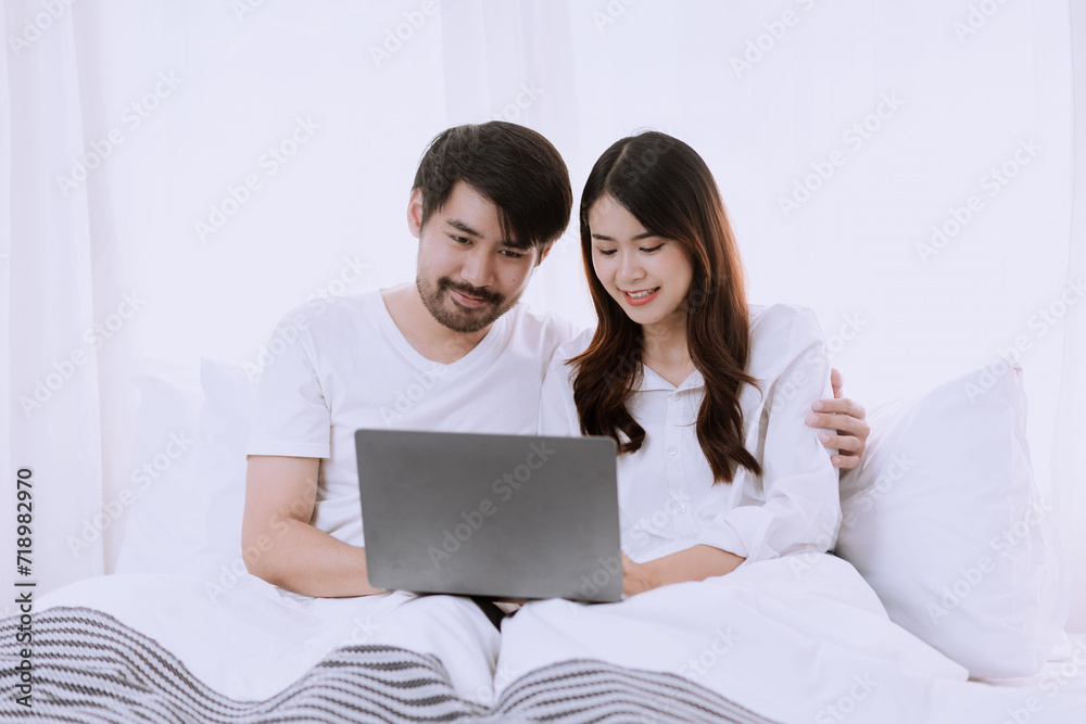 Happy asian man and woman using laptop sitting relaxed on a bed at home enjoy, Happy lover hug each other and smiling on the bed, Male and female couple concept. Happy asian man and woman using laptop sitting relaxed on a bed at home enjoy, Happy lover hug each other and smiling on the bed, Male and female couple concept.