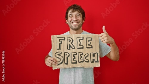 Cheerful young man flaunting his 'free speech' banner, giving the thumbs-up sign of approval! cool guy with a confident smile isolated against a vibrant red wall. photo