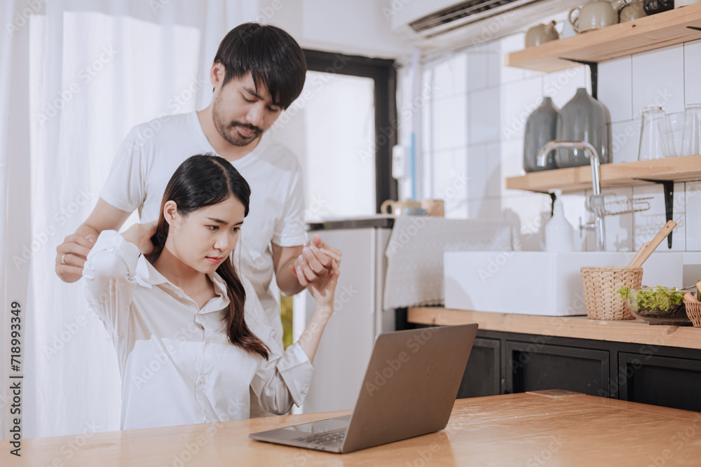 Happy love Asian young man and woman using laptop together in the kitchen relaxing at home.