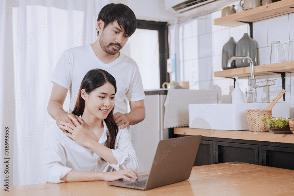 Happy love Asian young man and woman using laptop together in the kitchen relaxing at home. Happy love Asian young man and woman using laptop together in the kitchen relaxing at home.