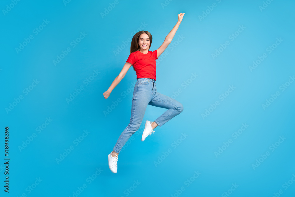 Full length photo of glad cheerful funky girl wear red trendy clothes flying forward dream raised hand isolated on blue color background