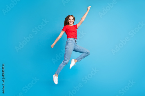 Full length photo of glad cheerful funky girl wear red trendy clothes flying forward dream raised hand isolated on blue color background