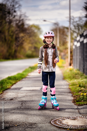 Schooler girl in helmet and full roller skating protection standing on street