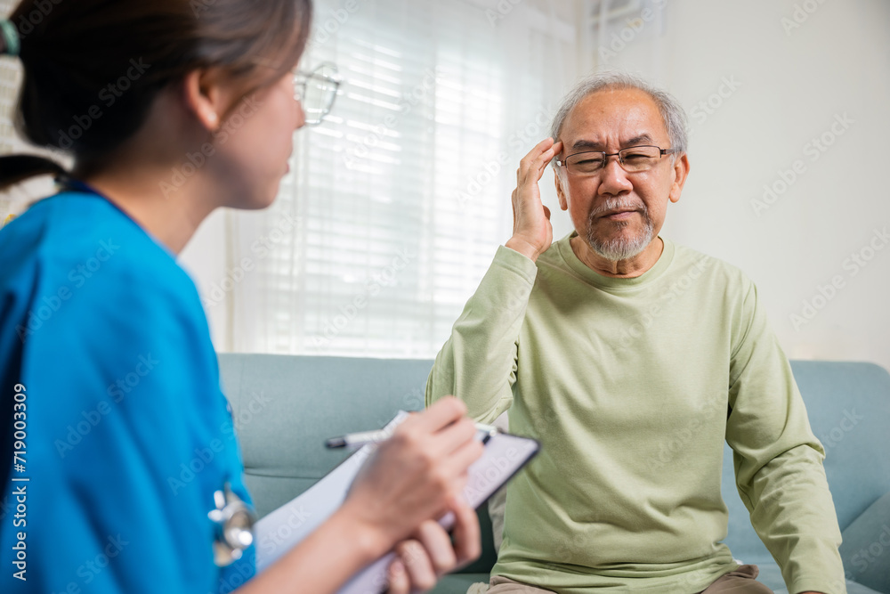 Obraz premium Asian senior old man patient have headache and woman nurse talking, checking up and recording current symptoms on clipboard in living room, Home healthcare and medical service