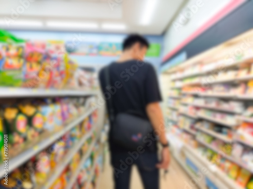 Blurred image of a man walking in a supermarket in a supermarket aisle with a back view of a man shopping in a department store. © Weerajit James
