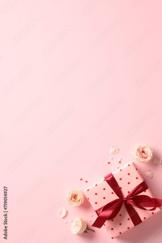 Valentine's day pink gift box with red ribbon bow, roses buds, confetti on pastel pink background. Flat lay, top view.