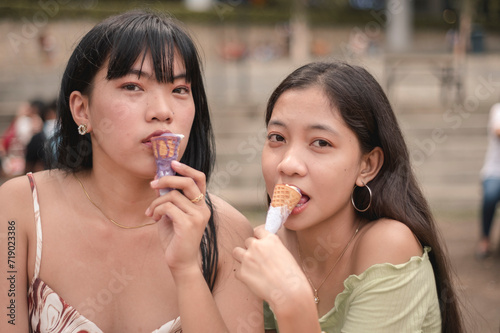 Two young Asian women savoring ice cream in a park  embodying leisure and friendship on a sunny day.
