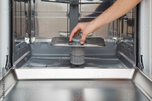 Young adult woman hand holding and putting clean filter in dishwasher. Closeup. Front view.