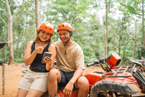 happy asian couple sitting on the atv while looking at the phone together