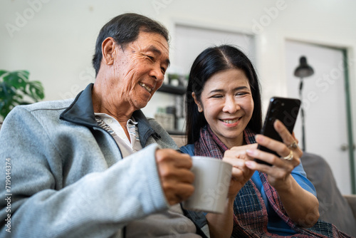 Retired elderly couple sits on couch drink tea and using mobile together and relax in their home. Senior Activity Concept