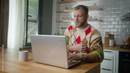 Adult man sit in kitchen suffering chest pain, holding massaging his chest while research to solution on internet with laptop. Male trouble breathing stroke at home. Health problems concept photo