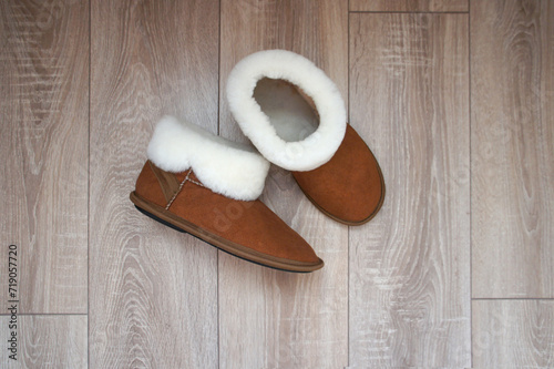 Brown ugg boots with white fur. Home slippers on parquet floor in the room.  photo