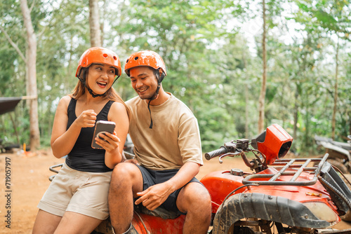 asian woman pointing on the phone while sitting on the atv together with her man