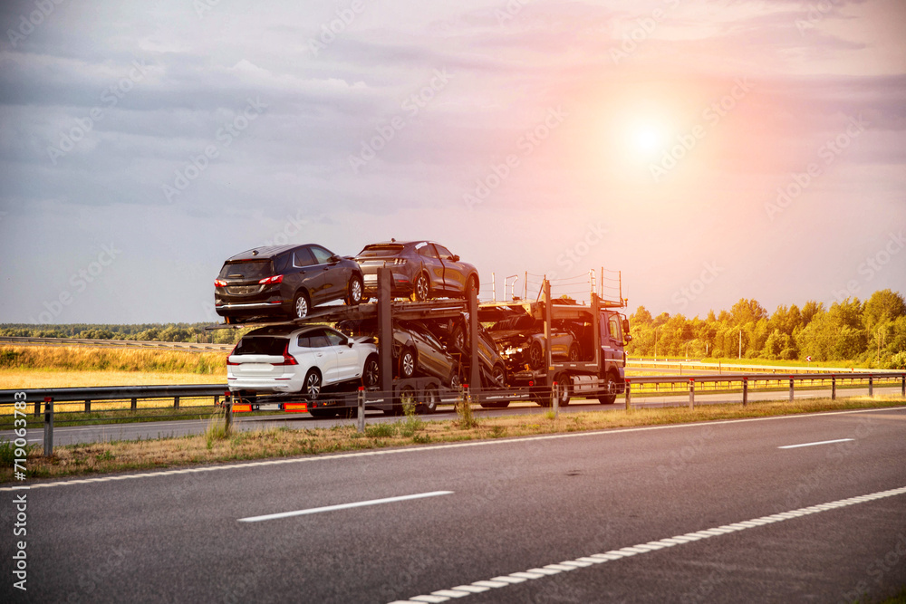 An auto transporter semi-trailer truck transports broken damaged cars from Europe in the summer against a sunset background. Car import and export concept, shipping
