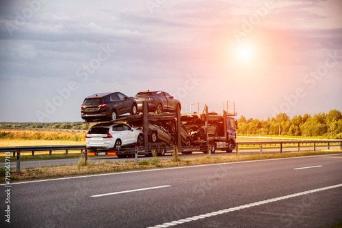 An auto transporter semi-trailer truck transports broken damaged cars from Europe in the summer against a sunset background. Car import and export concept, shipping