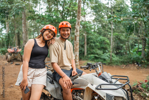 beautiful asian women leaning on the mans shoulder while standing beside the atv with the phone at her hand