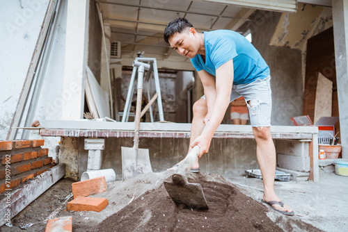 Asian man doing construction work is mixing cement with sand using a hoe for the walls of a house