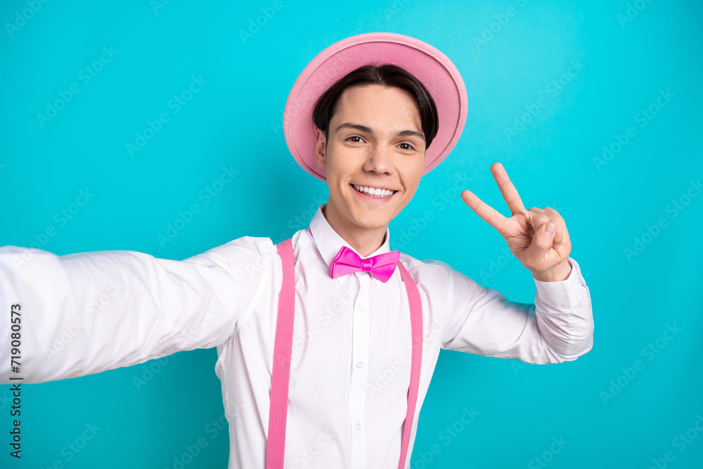 Photo portrait of pretty young male take selfie photo show v-sign wear trendy pink outfit isolated on cyan color background Photo portrait of pretty young male take selfie photo show v-sign wear trendy pink outfit isolated on cyan color background