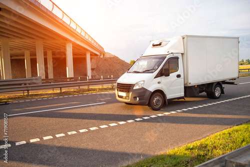 A low-tonnage commercial refrigerated van transports perishable products in the summer on a country road against the backdrop of sunset. Industry, business photo