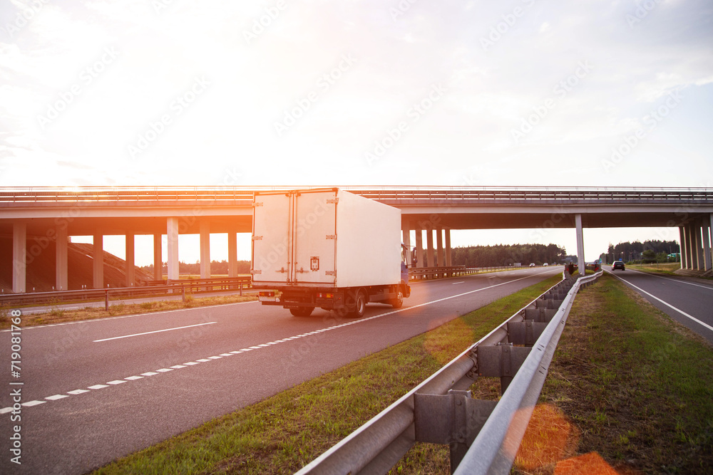 Fototapeta premium A low-tonnage commercial refrigerated van transports perishable products in the summer on a country road against the backdrop of sunset. Industry, business